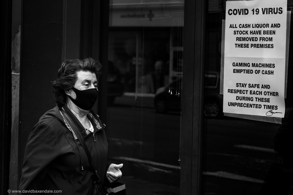 a woman with grey hair walks by a business shut by COVID-19 restrictions