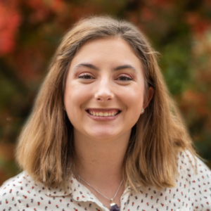 Picture of a girl smiling against a blurred background of fall leaves
